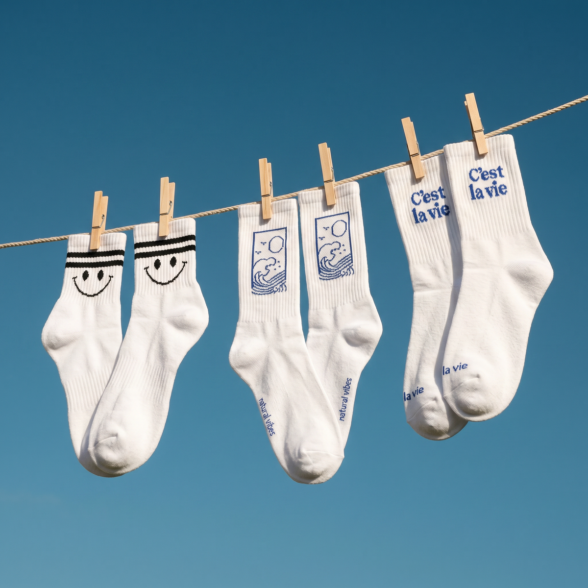 Drei Paar weiße Natural Vibes Tennissocken mit Motiven, die nach dem Waschen auf der Leine hängen.