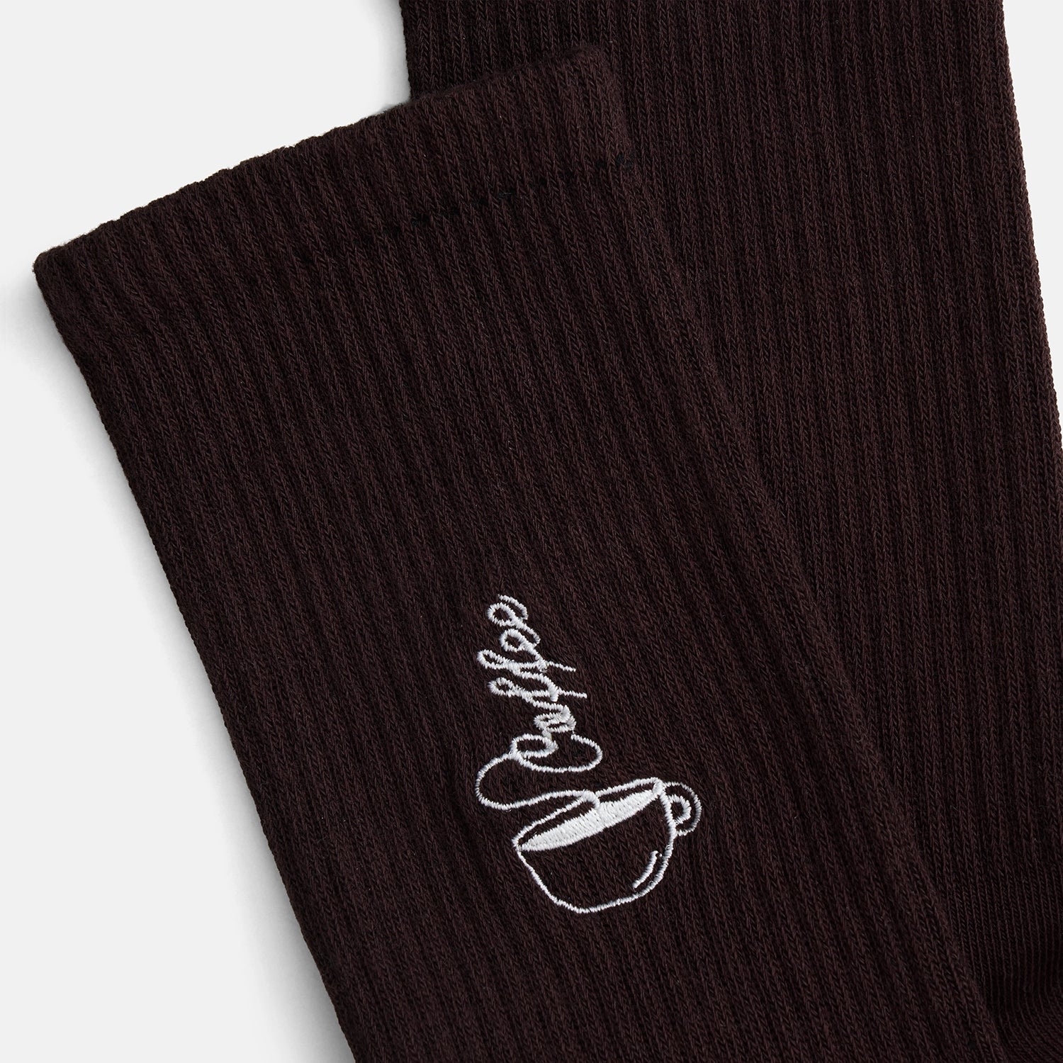 Kaffee-Socken von Natural Vibes. Detailaufnahme der weißen Stickerei einer Kaffeetasse mit "Coffee" Schriftzug auf dunkelbraunen Bio-Tennissocken.