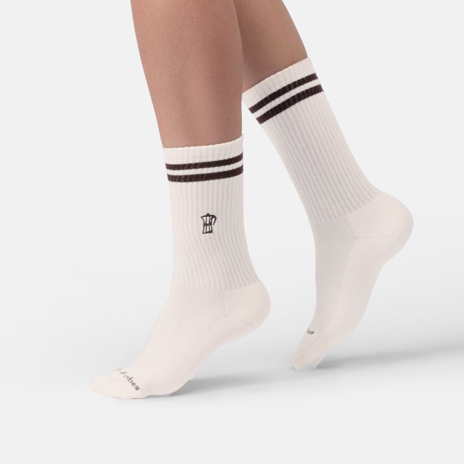 Person trägt naturweiße Bio-Tennissocken mit Mokkakannen-Stickerei und braunen Streifen.