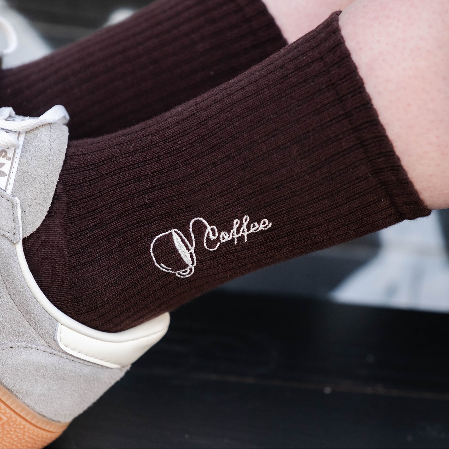 Dunkelbraune Bio-Tennissocken mit Kaffee-Stickerei kombiniert mit grauen Sneakern.