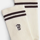 Detailaufnahme der Mokkakannen-Stickerei auf naturweißen Bio-Tennissocken mit braunen Streifen.