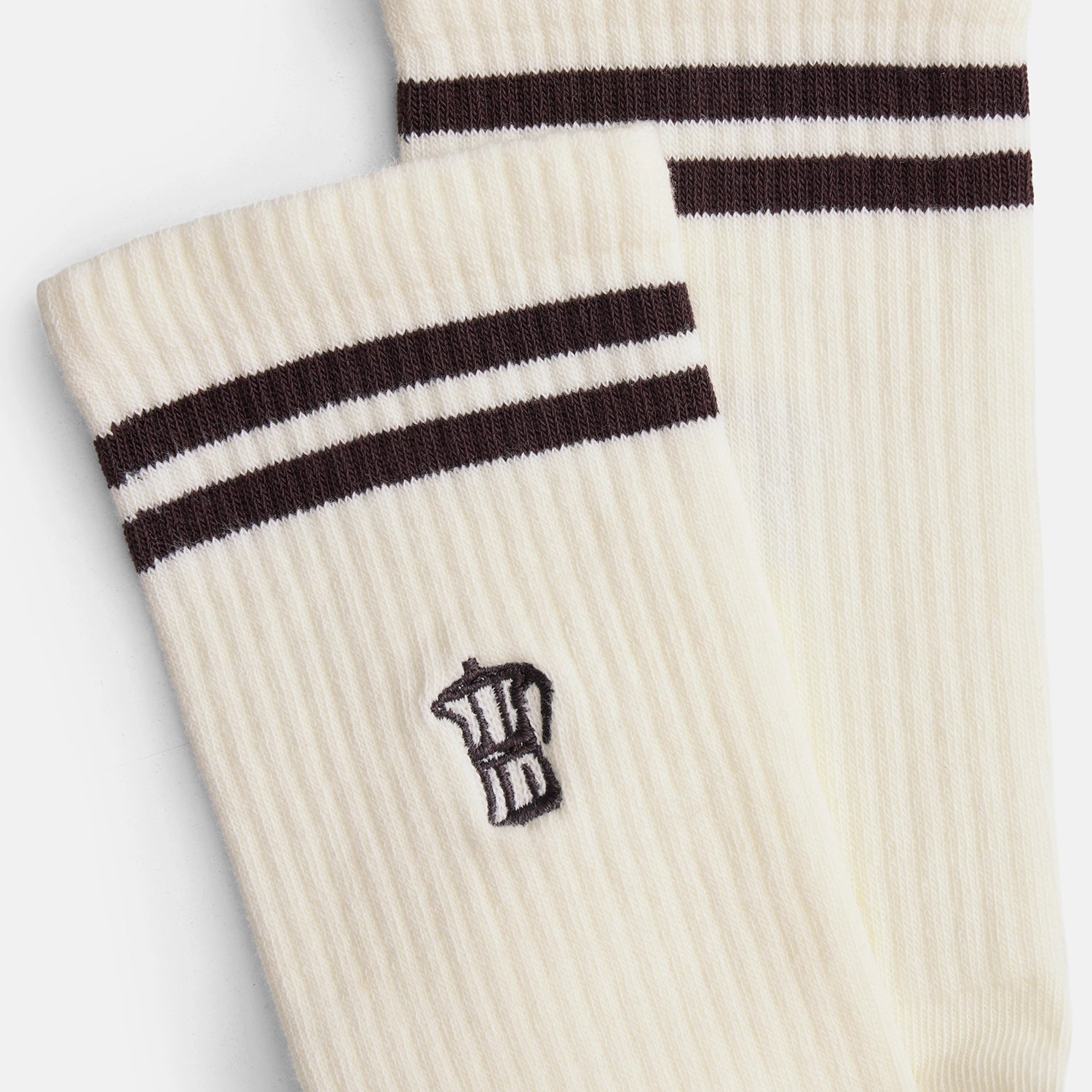 Detailaufnahme der Mokkakannen-Stickerei auf naturweißen Bio-Tennissocken mit braunen Streifen.