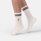 Person trägt naturweiße Bio-Tennissocken mit Mokkakannen-Stickerei und braunen Streifen.