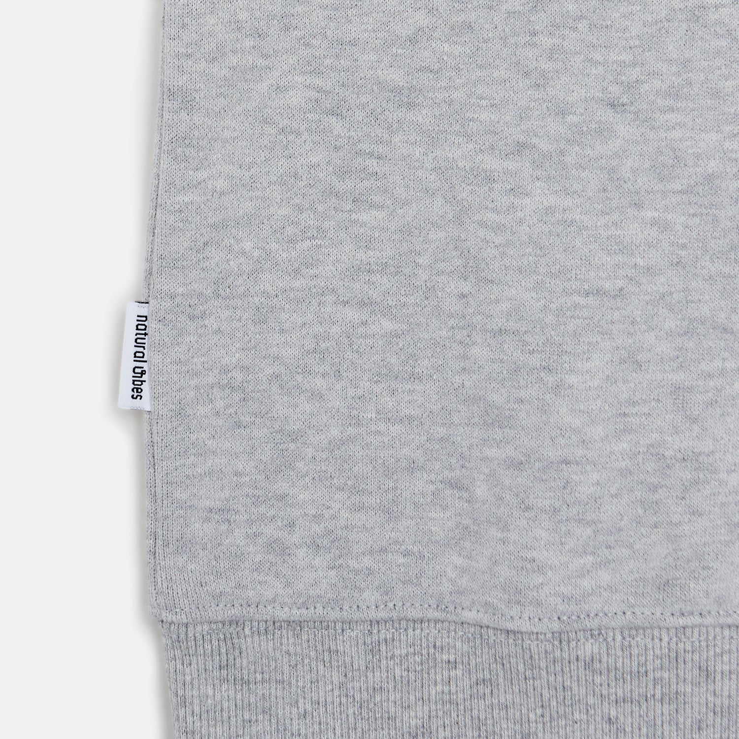Detailansicht des gerippten Saums und gewebten Logo-Labels am hellgrauen Bio-Baumwoll-Sweater Panda. 