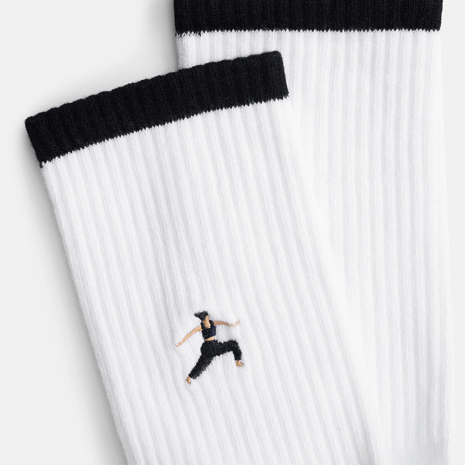 Detailansicht der Stickerei einer Person in Kriegerpose auf dem Schaft der weißen Warrior Tennissocken  – Natural Vibes Clothing